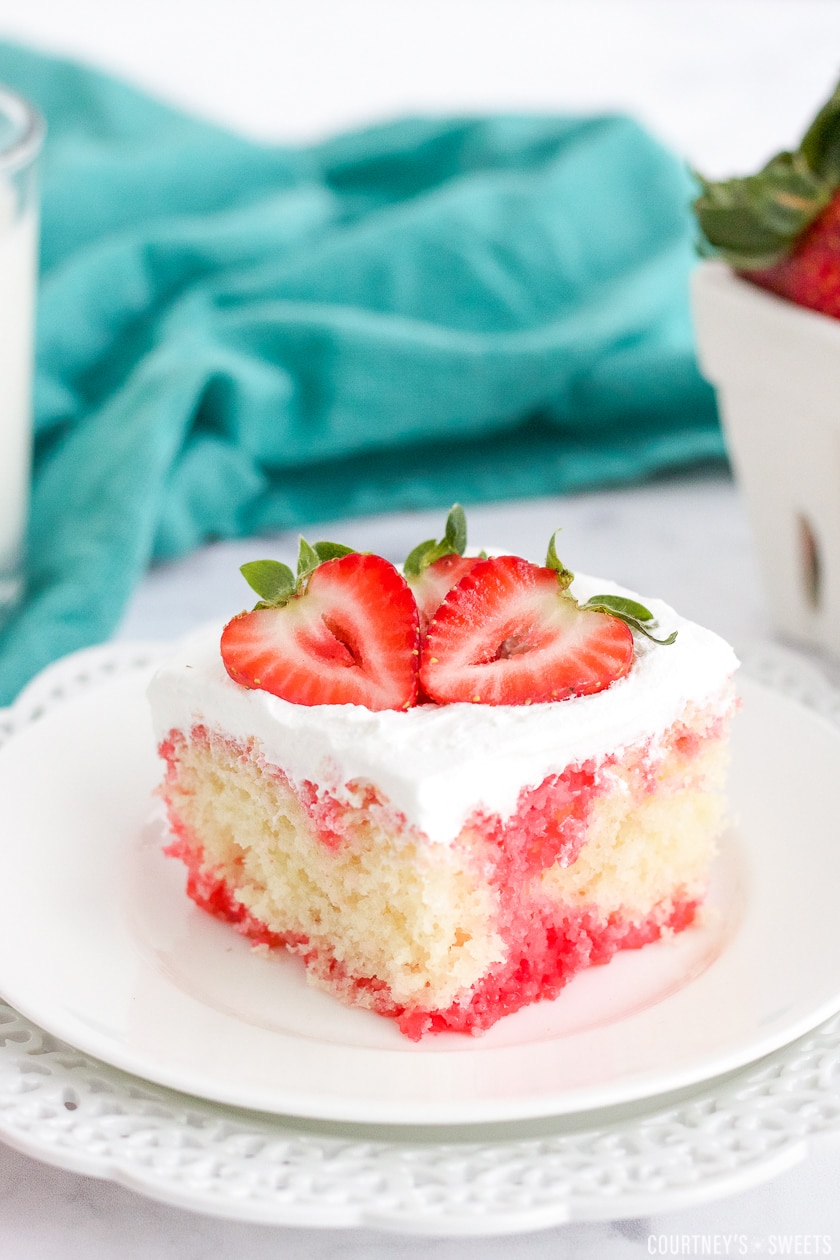 strawberry poke cake on a white plate with a strawberry on top.