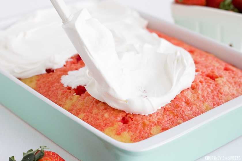 spatula spreading whipped topping onto a jello poke cake.