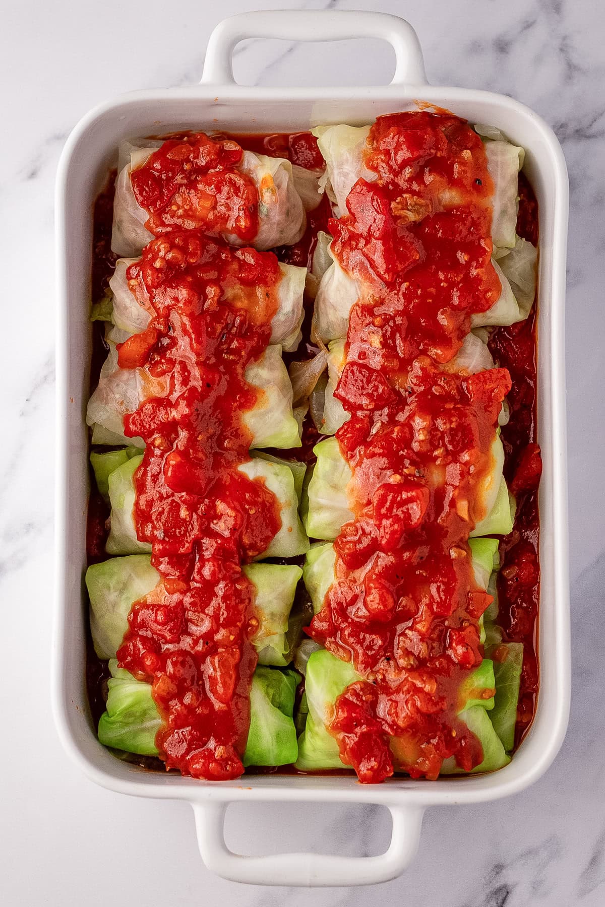 sauce over raw stuffed cabbage rolls in casserole dish.