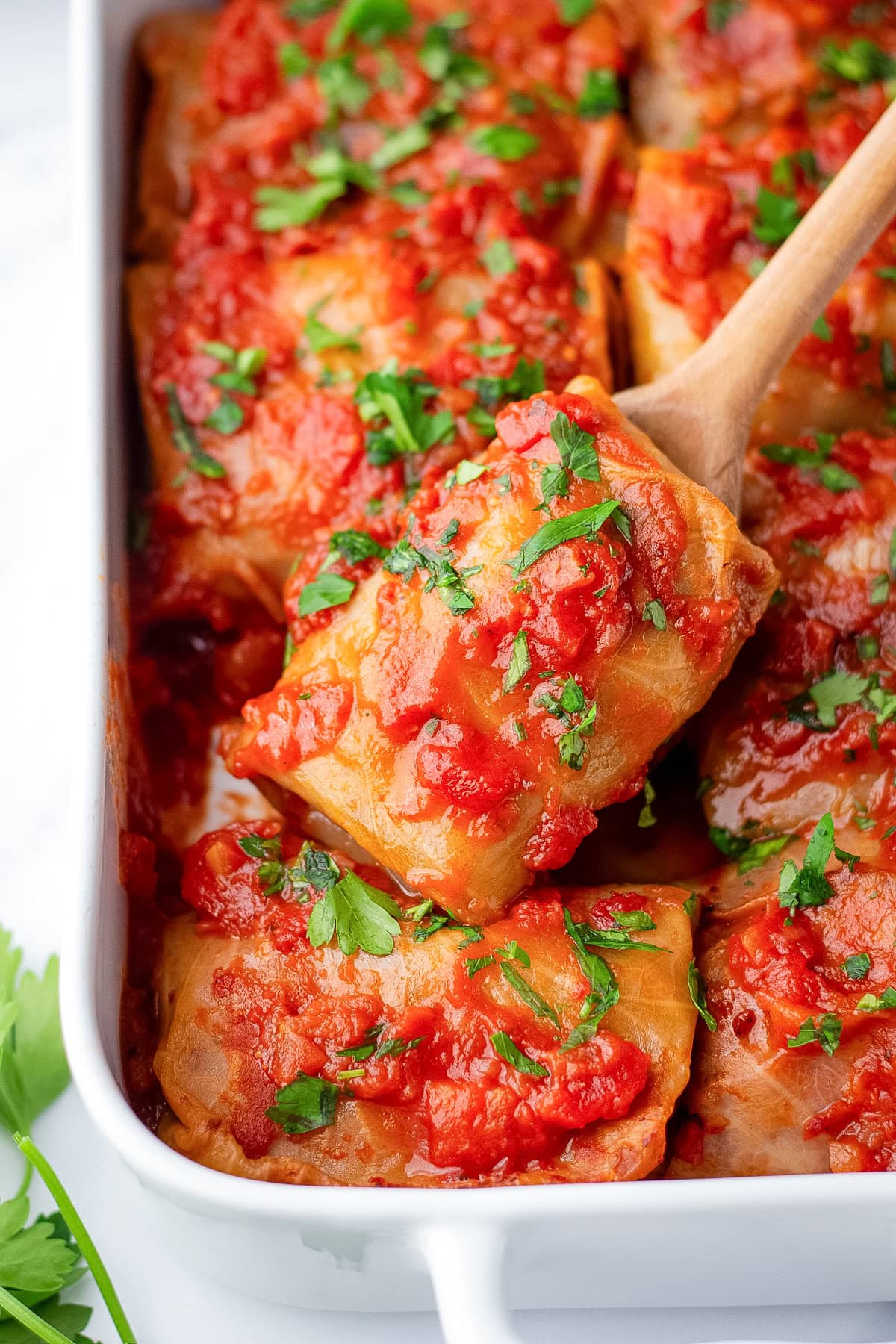 stuffed cabbage rolls in a casserole dish with a spoon showing one closer.