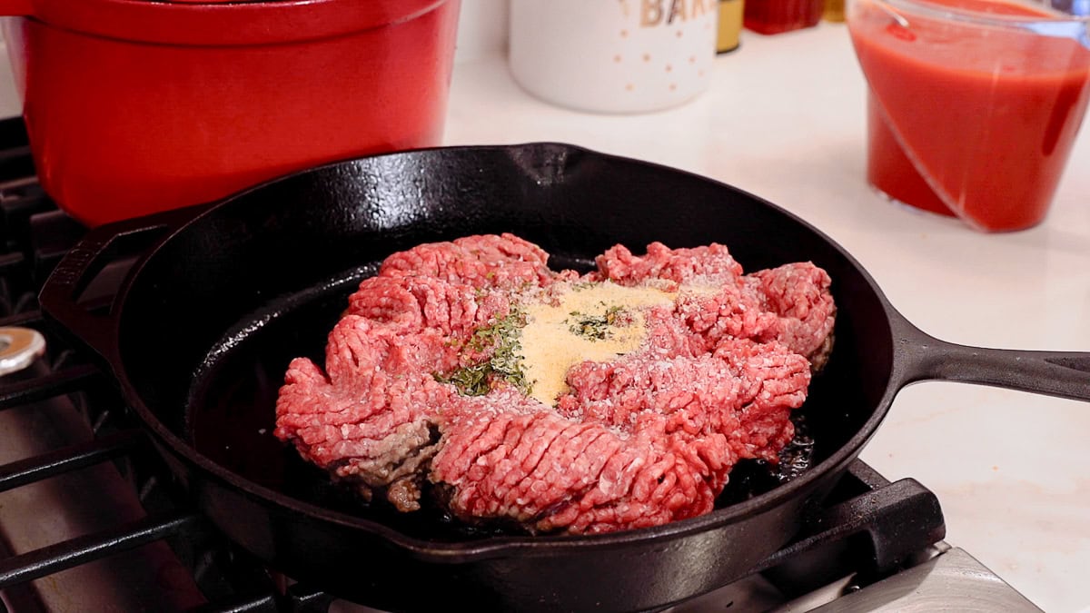 ground beef in a cast iron skillet with seasonings ready to cook.