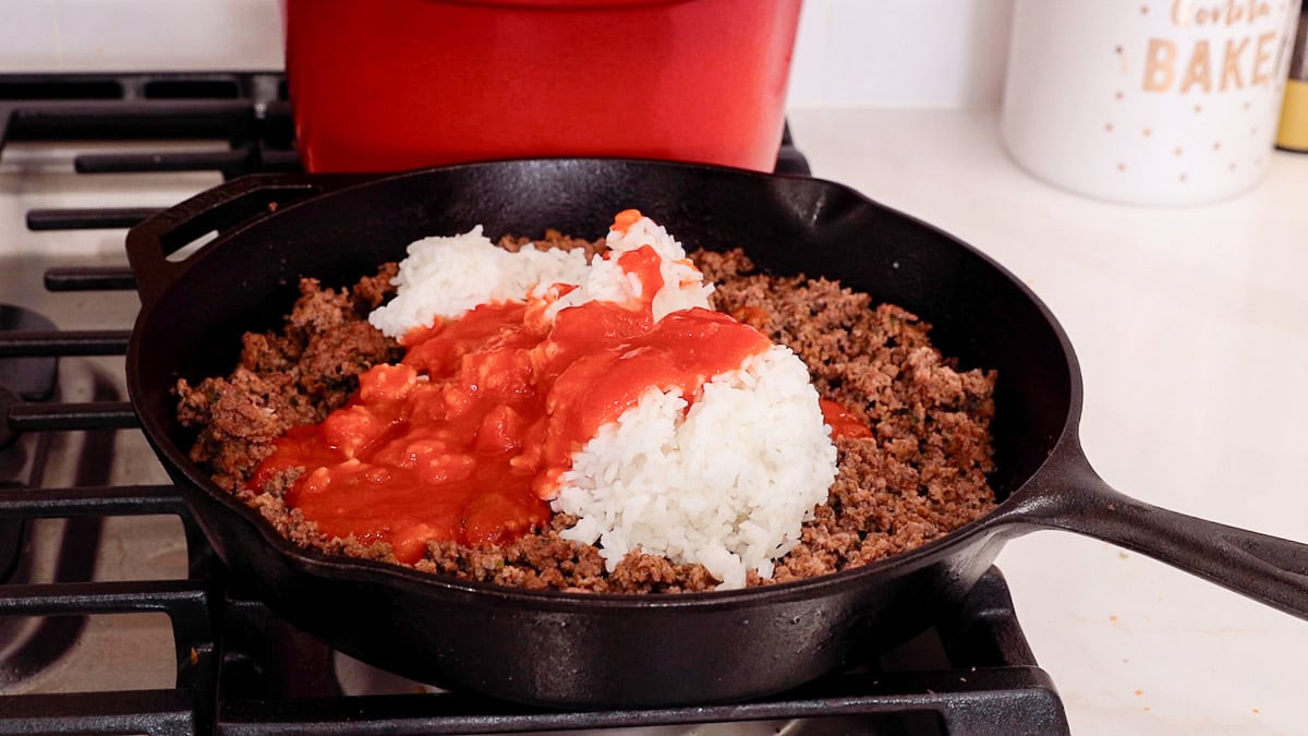 rice and tomato sauce added to ground beef in a cast iron skillet.