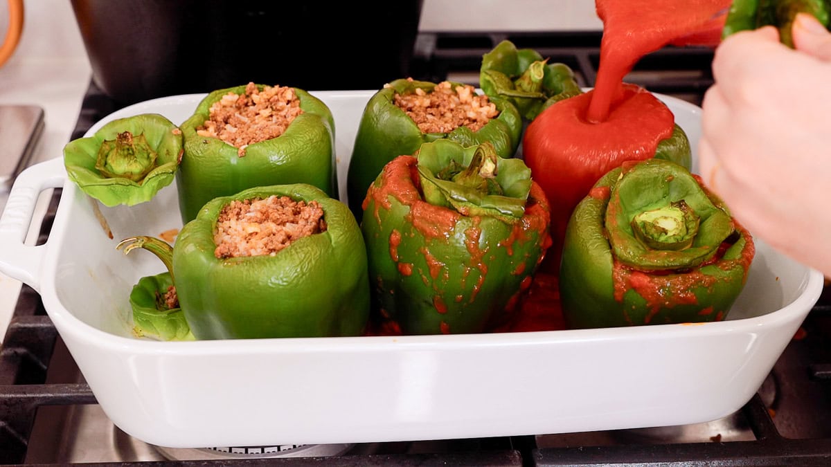 pouring sauce over stuffed bell peppers.