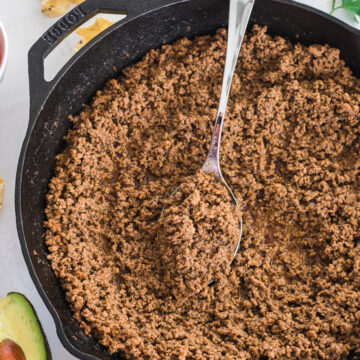 ground beef taco meat in cast iron skillet with scattered chips around.