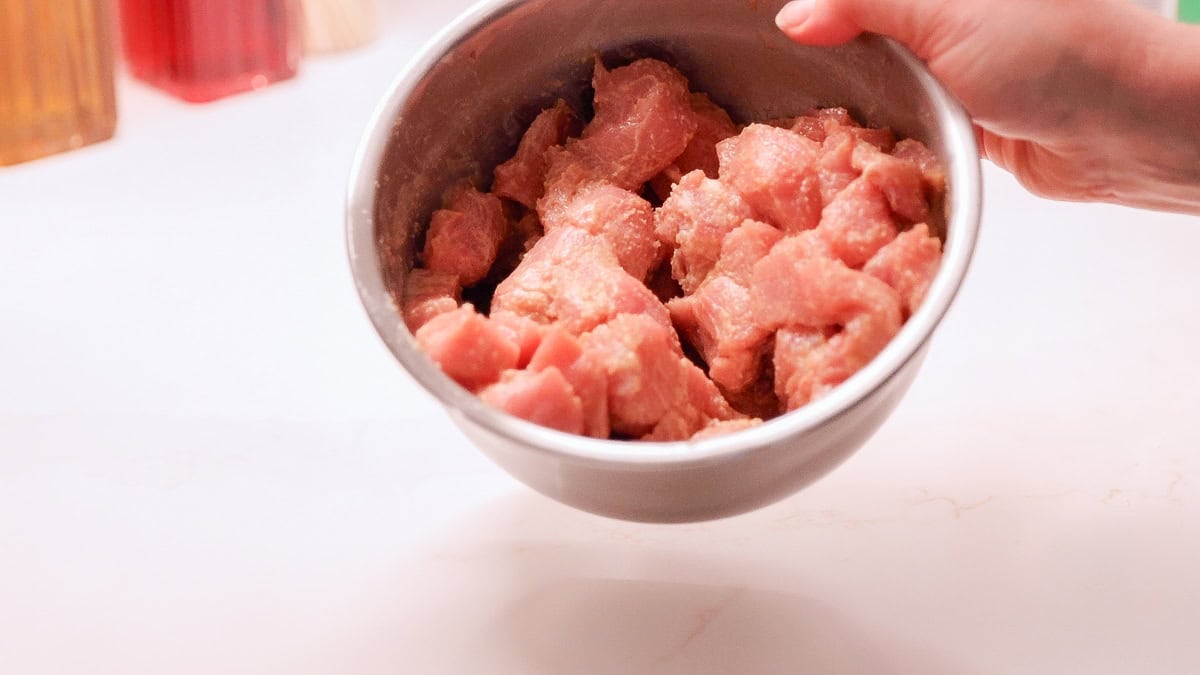 bowl of pork chop covered in cornstarch, oil, seasonings, and soy sauce with a bit of water to marinate quickly, velveting.