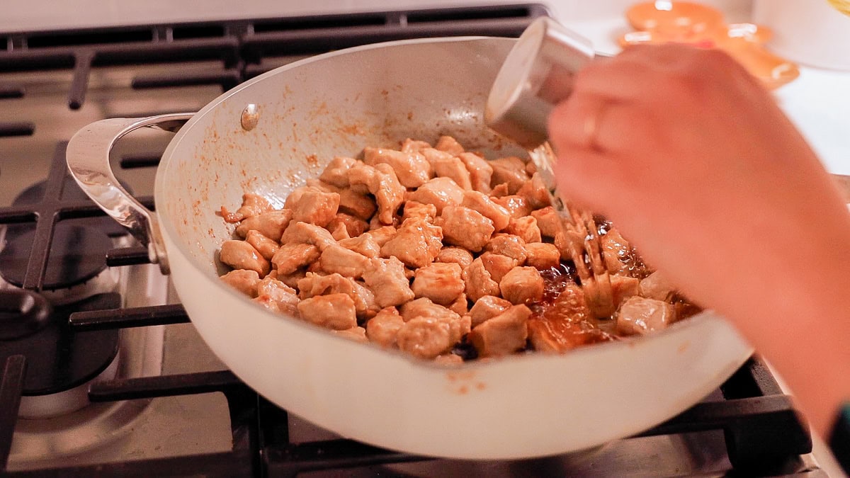 hand pouring mirin into pan over pork.