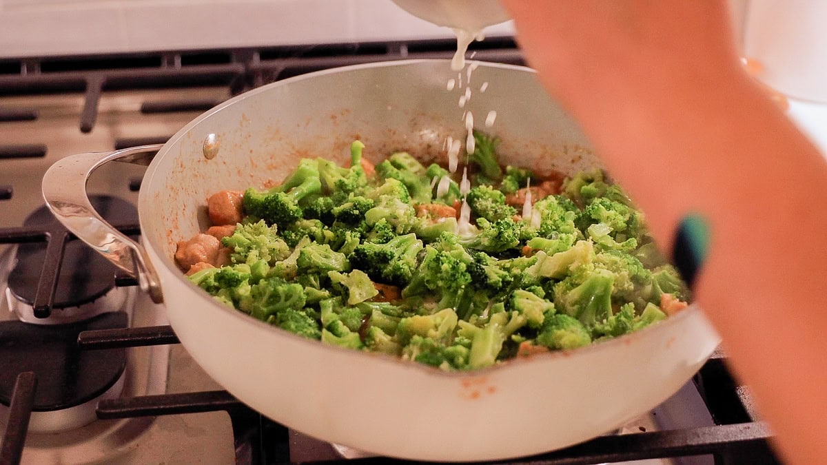 hand pouring cornstarch slurry over broccoli and pork stir fry.