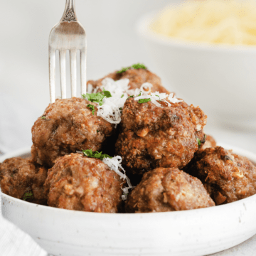 fork sticking into a meatball on a white low bowl full of air fryer meatballs.