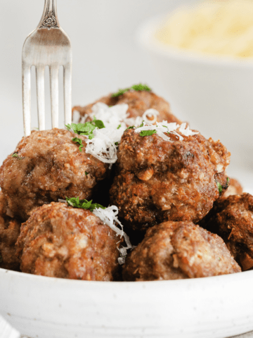 fork sticking into a meatball on a white low bowl full of air fryer meatballs.