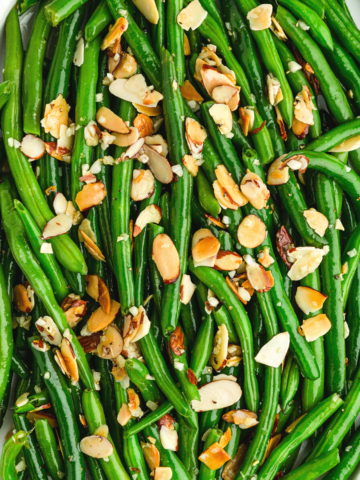 overhead photo of green beans almondine on a white platter.