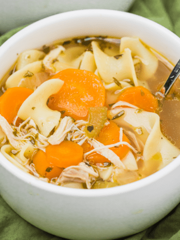 instant pot chicken noodle soup in a white bowl with a spoon and a green napkin.